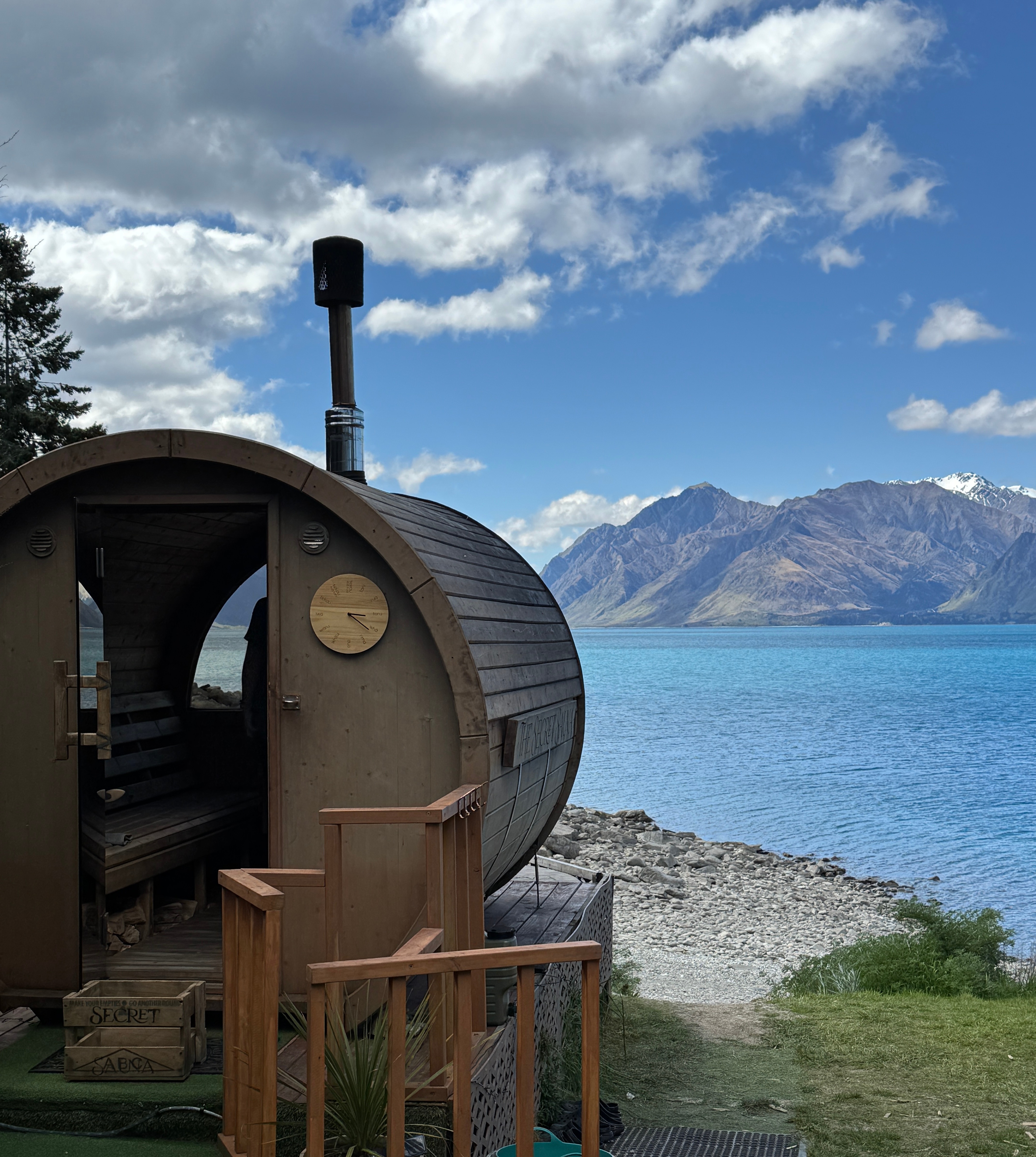 A lakeside sauna looking out over a turquoise alpine lake and snow-capped mountains