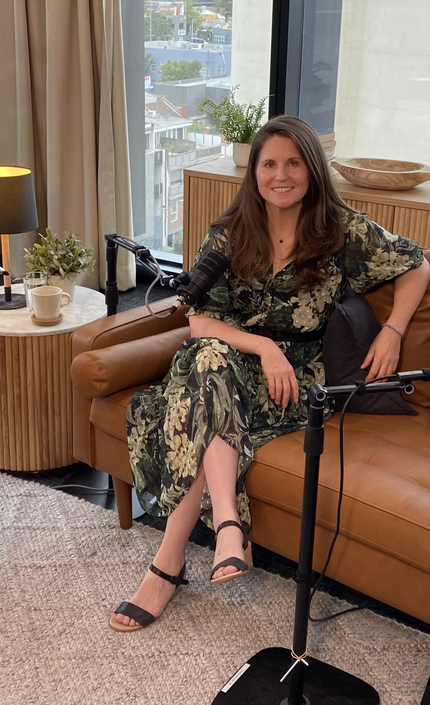 Kirsty Dunphey in a green floral dress seated with podcast microphones during a recording
