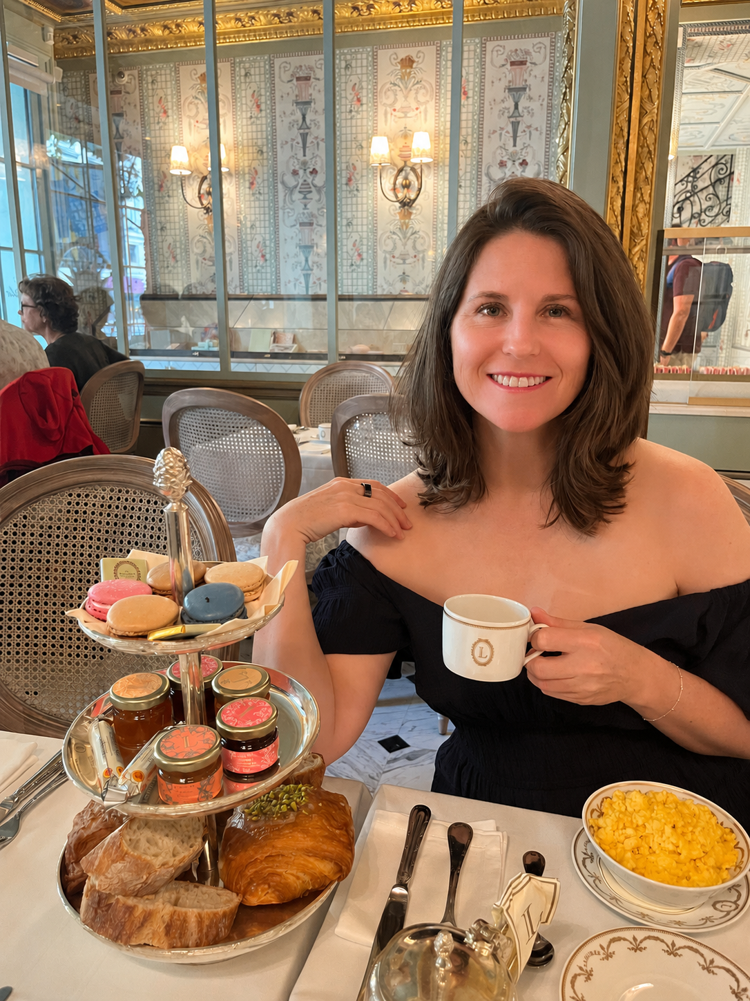 Kirsty Dunphey enjoying an elegant afternoon tea, holding a monogrammed cup beside a tiered stand of macarons and pastries at Ladurée in Paris