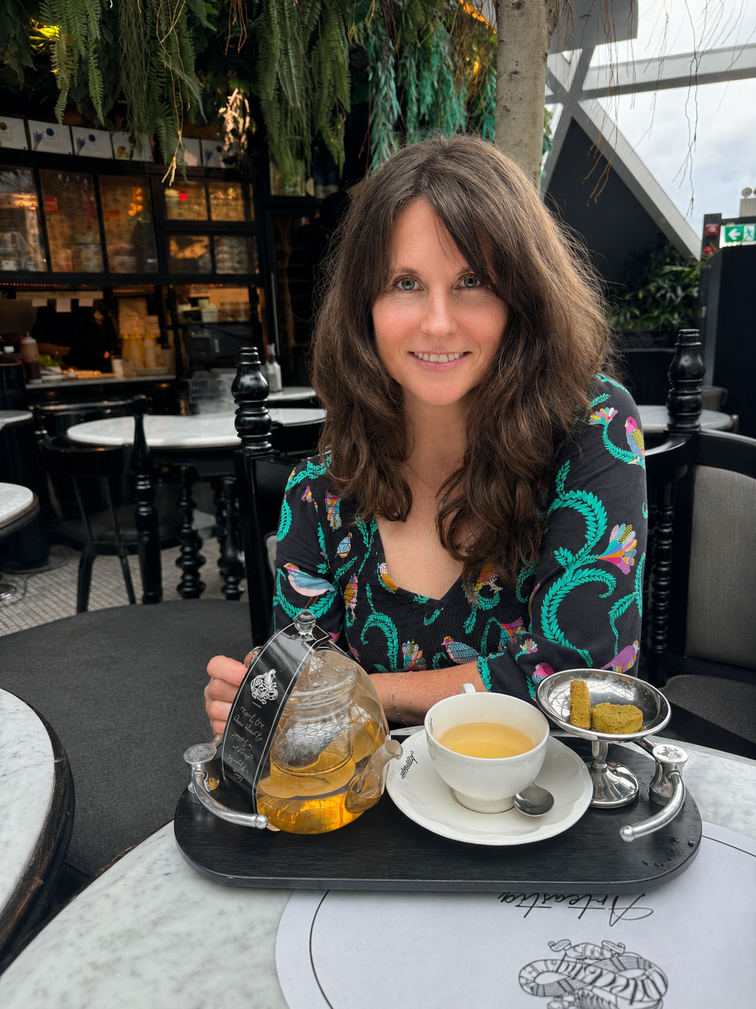 Kirsty Dunphey seated at a cafe with a glass teapot of golden tea and a cup on a tray